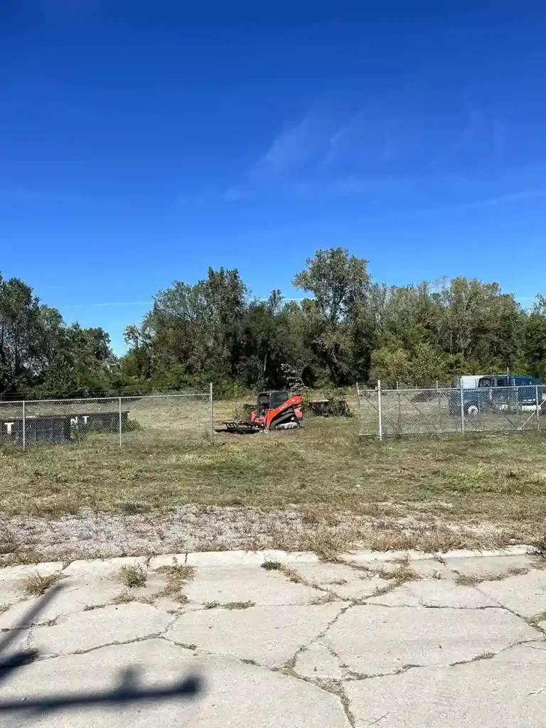 Better Way Land Management LLC crew operates orange skid steer clearing overgrown vegetation from fenced commercial lot in Ohio