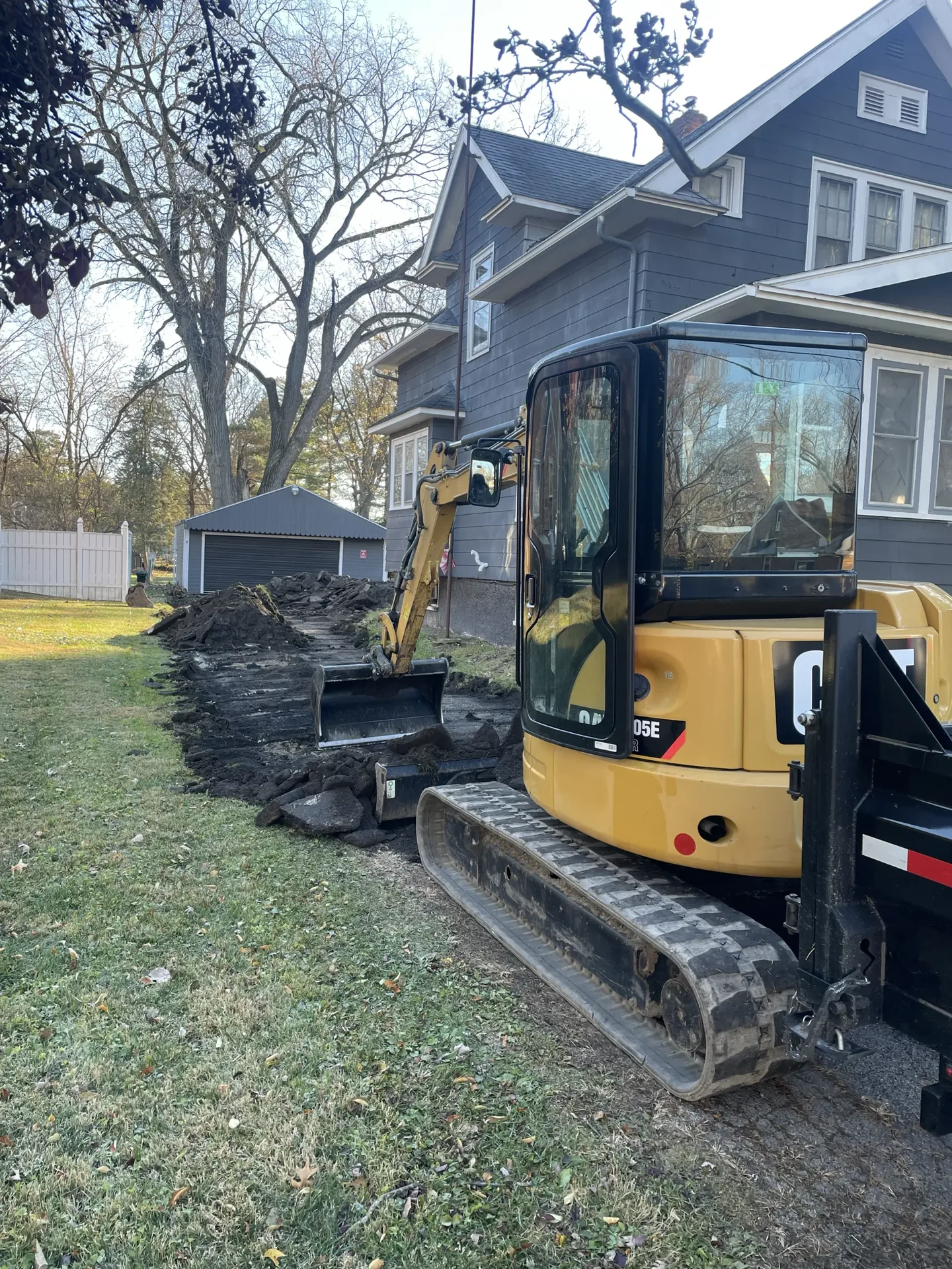 Better Way Land Management LLC operator using CAT mini excavator to dig trench alongside residential home in OH