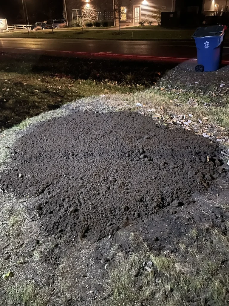 Better Way Land Management LLC fresh excavated soil pile on residential lawn during nighttime site preparation work in Ohio