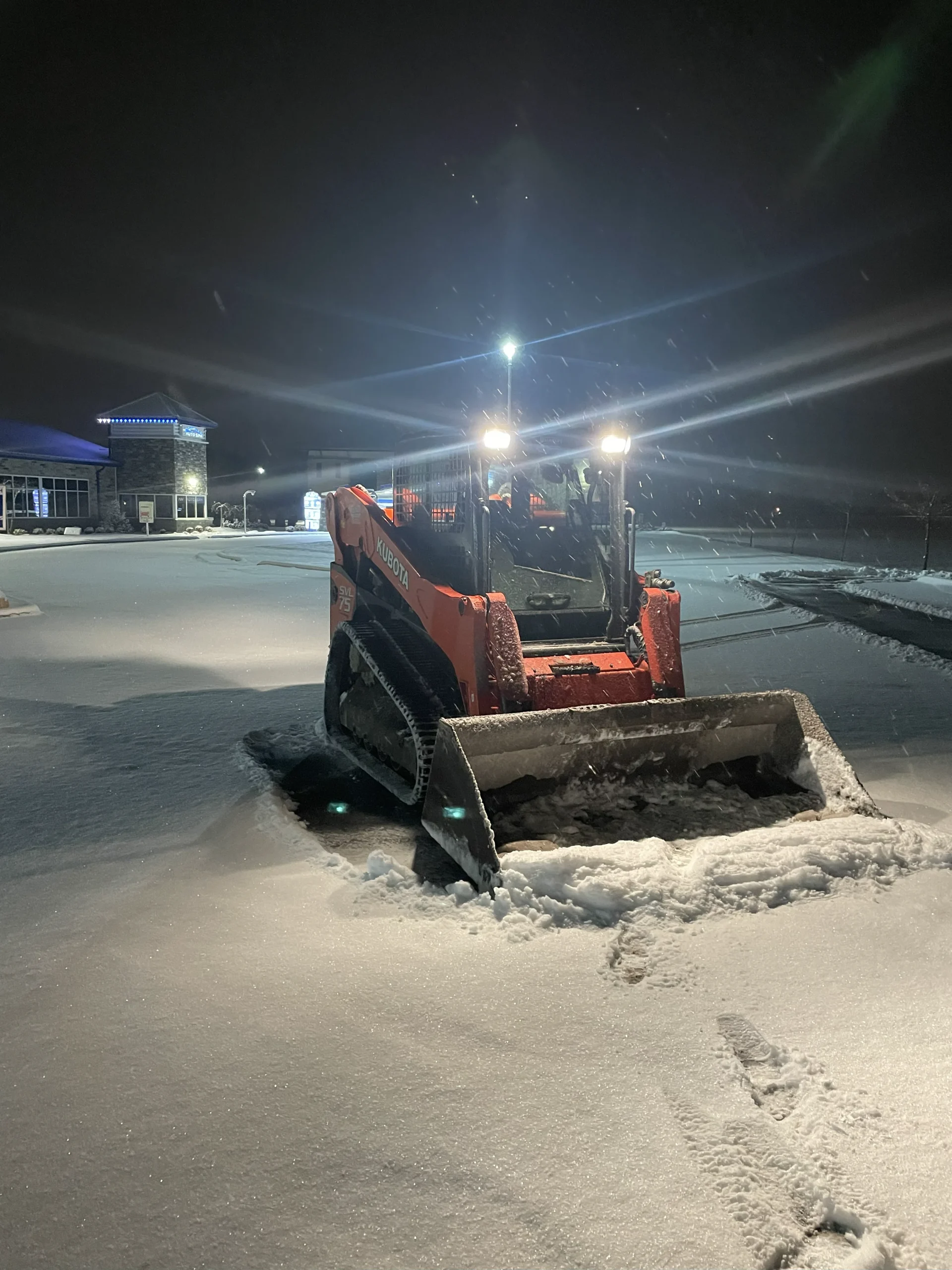 Better Way Land Management LLC Kubota tracked skid steer clearing snow from commercial parking lot at night in Ohio