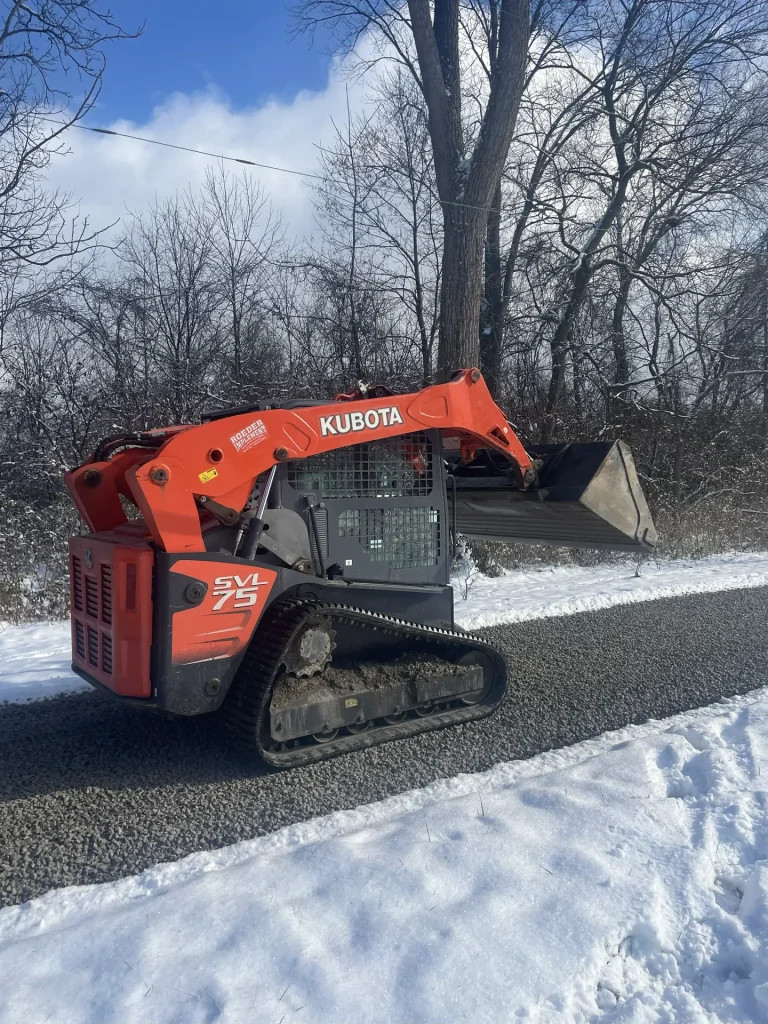 Better Way Land Management LLC Kubota SVL75 compact track loader with raised bucket on cleared gravel driveway in snowy Ohio winter setting