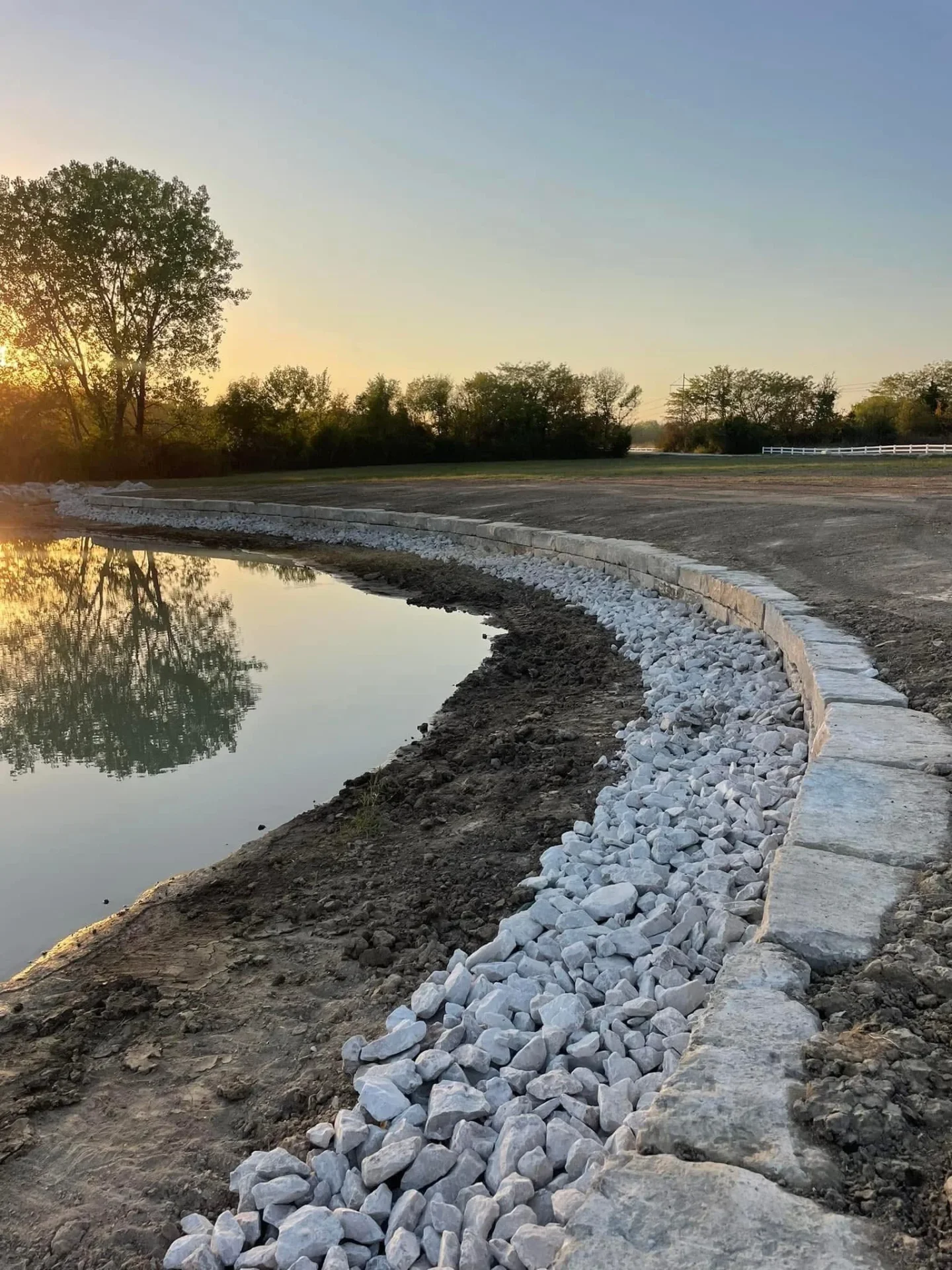 Better Way Land Management LLC completed pond shoreline with white limestone riprap erosion control along curved bank at sunset in OH