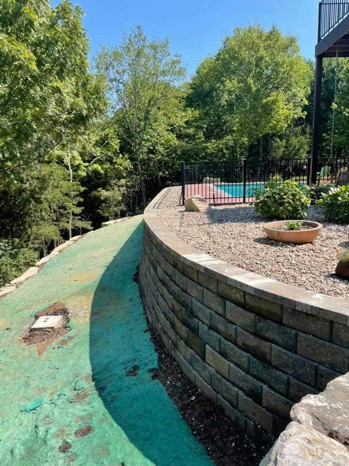Better Way Land Management curved block retaining wall with fresh hydroseeding on slope near residential pool area
