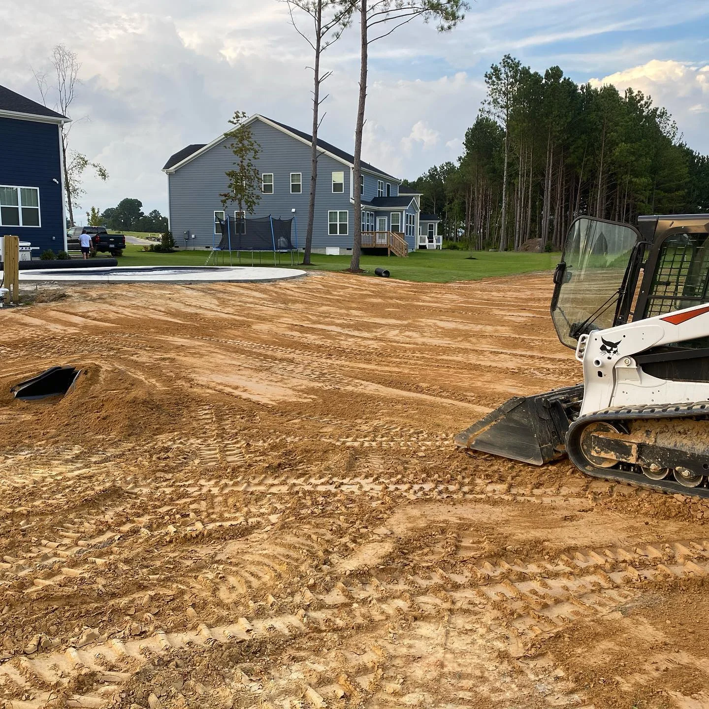 Better Way Land Management LLC skid steer track loader providing grading services in Northwest Ohio leveling dirt lot near residential home