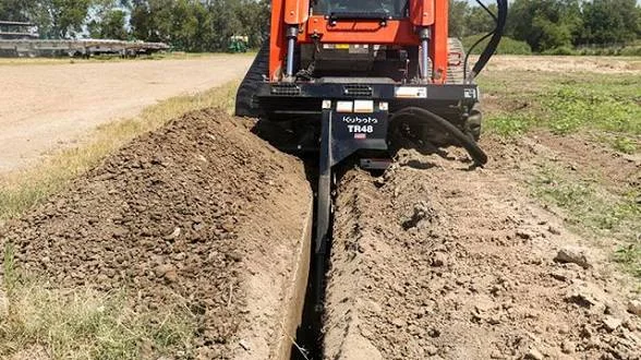 Better Way Land Management LLC Kubota TR48 trencher attachment digging straight trench through soil on outdoor worksite