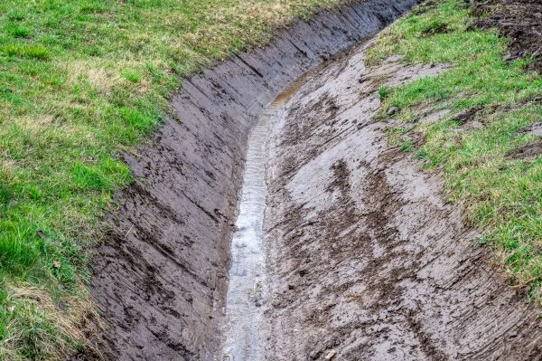 Better Way Land Management LLC freshly excavated drainage ditch with muddy walls and water flowing through grassy field channel
