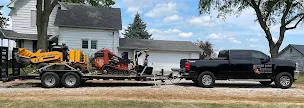 Better Way Land Management LLC black pickup truck hauling flatbed trailer loaded with Ditch Witch skid steer and Dynapac roller equipment