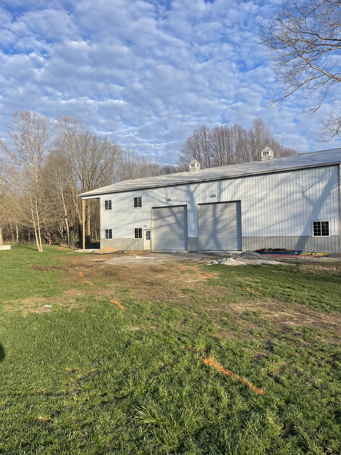 Better Way Land Management LLC newly constructed gray metal pole barn with dual large garage doors and cupolas in rural setting