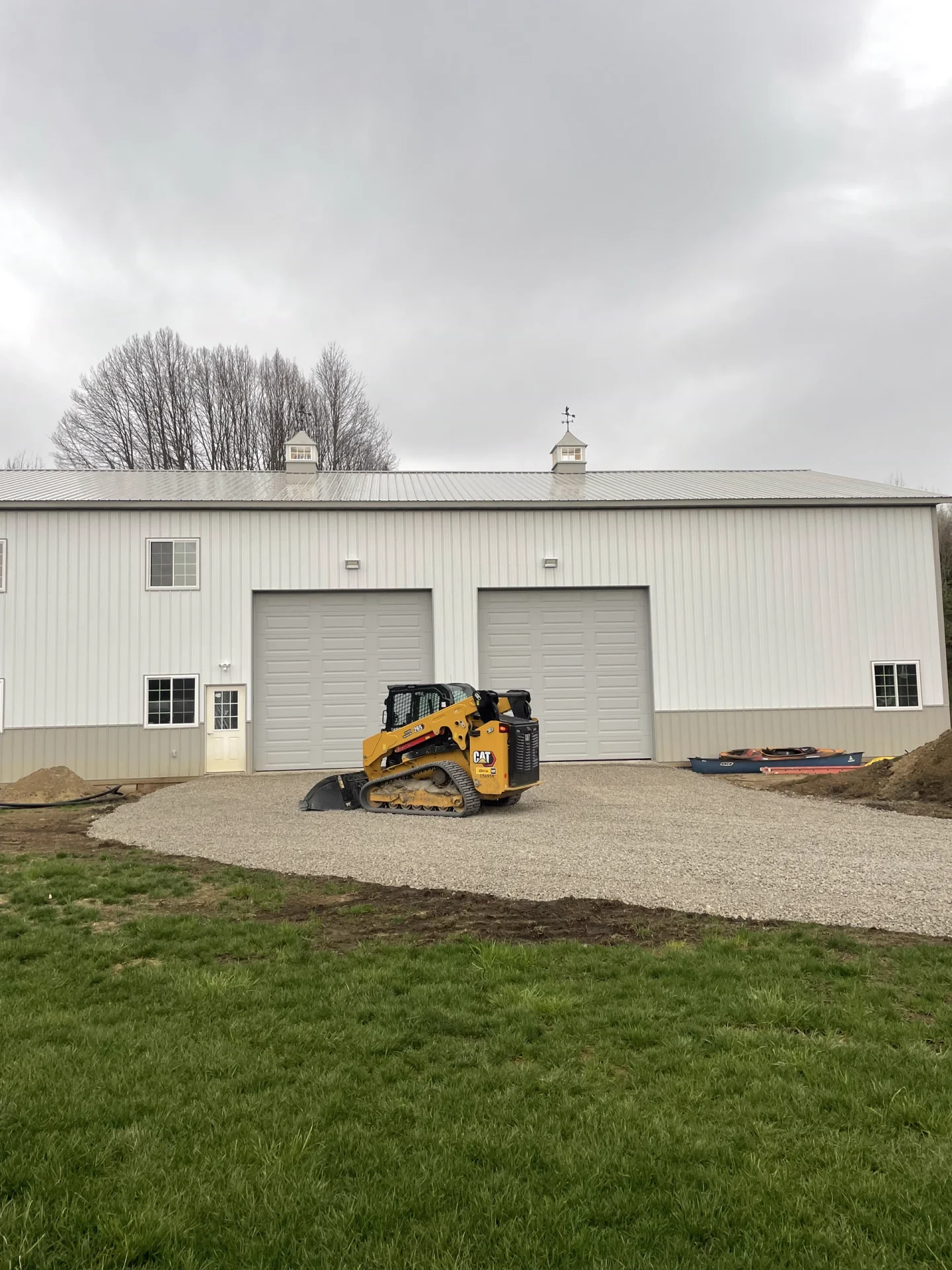 Better Way Land Management LLC CAT tracked skid steer spreading gravel driveway in front of large white metal pole barn building